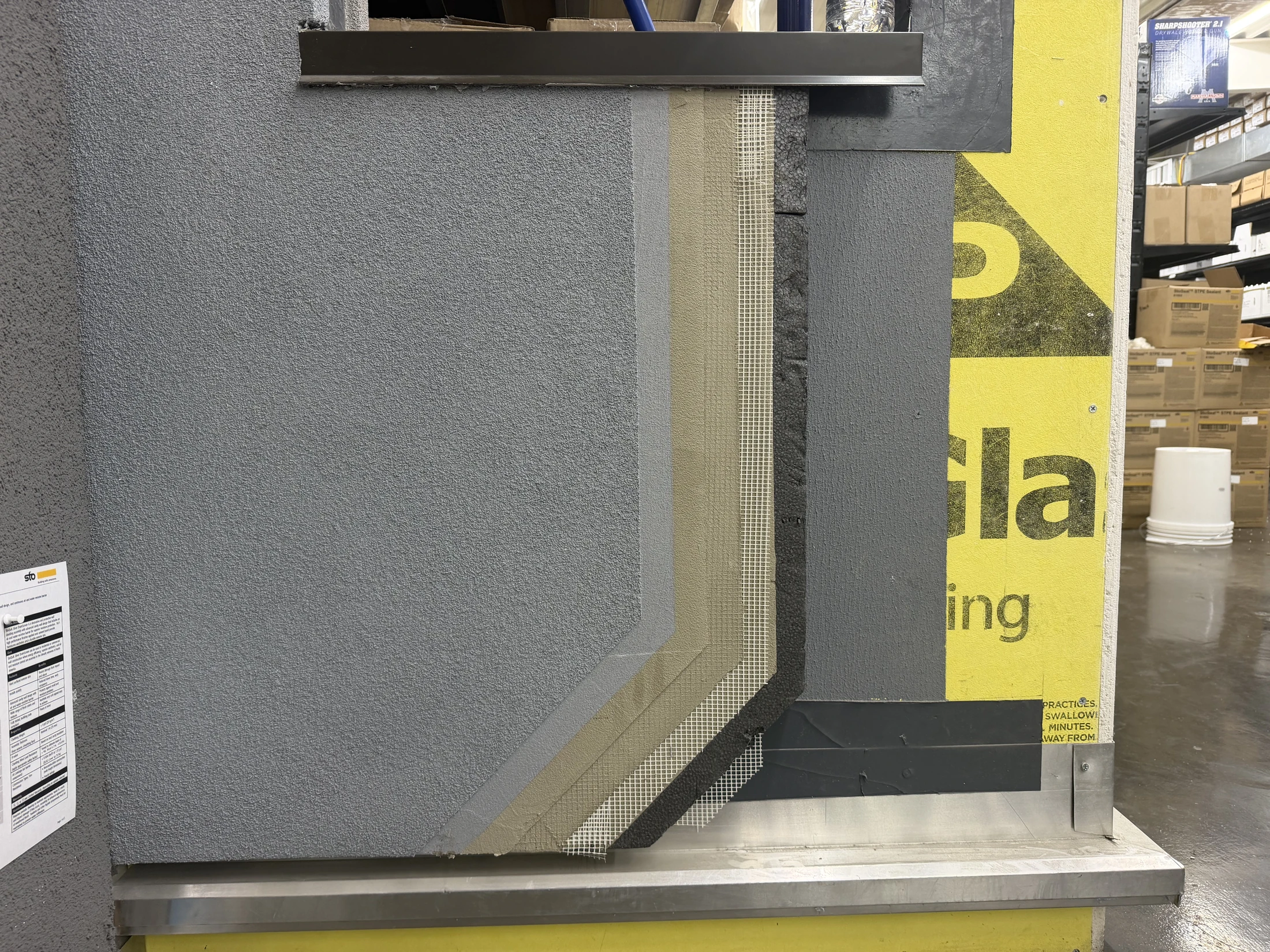 Stepped wall-system display at HSS showing the exposed layers from sheathing through insulation, mesh and finish